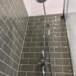 Modern bathroom shower with gray tiles and stainless steel fixtures.