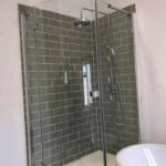 A corner shower stall with glass doors and grey porcelain tiling.
