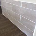 A neatly porcelain tiled wall meets a textured floor, showcasing a clean and modern corner finish.
