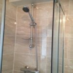 A modern shower with a height-adjustable showerhead, glass door, and porcelain tiling.