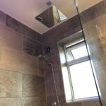 Modern shower with an overhead rainfall showerhead and a handheld showerhead, featuring bathroom tiling and a window.
