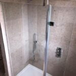 Modern walk-in shower with glass door, featuring dual showerheads and natural stone tiling walls.