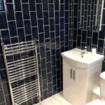 A modern bathroom corner with porcelain tiling, a pedestal sink, and a heated towel rail.