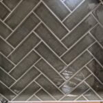 Herringbone ceramic tiling backsplash in a kitchen with under-cabinet lighting.