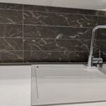 A modern kitchen sink with a sleek faucet against natural stone tiling backsplash.