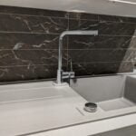 Modern kitchen sink with a stainless steel faucet against a dark marble backsplash, complemented by elegant natural stone tiling.