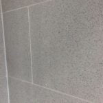 Grey speckled porcelain tiling with white grout lines.