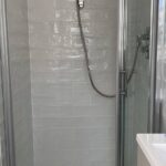 A modern walk-in shower with glass doors and pale porcelain tiling walls.