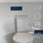 A modern bathroom with a white toilet and white porcelain tiling featuring a horizontal line of blue accent tiles.