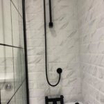 A modern bathroom shower with black fixtures and white ceramic tiling.