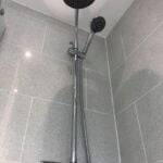 Modern shower system with a fixed overhead shower and an adjustable handheld showerhead against a porcelain tiled wall.