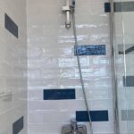 A modern shower with white and blue mosaic tiling and a glass door.
