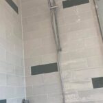 A partially wet porcelain-tiled shower wall with a visible metal grab bar.