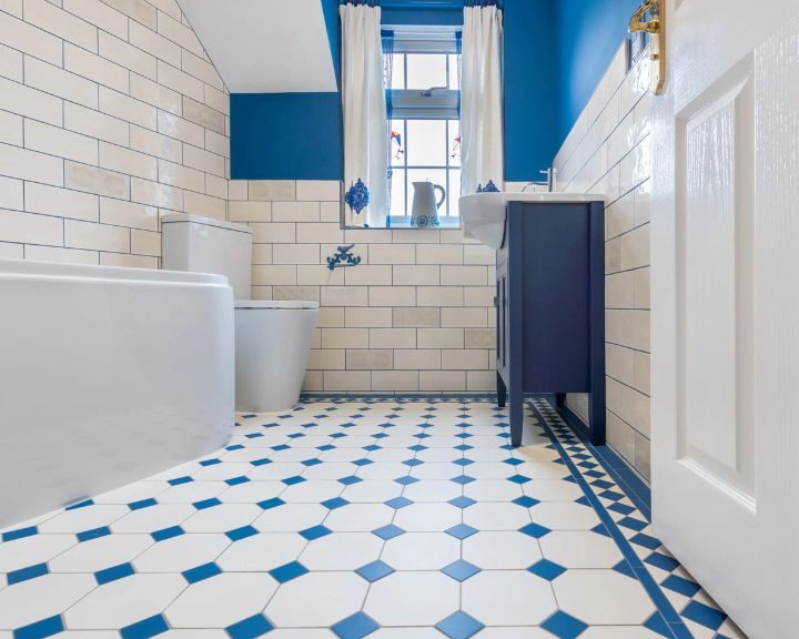 Modern bathroom with blue and white mosaic tiling, featuring a freestanding bathtub, toilet, and sink.