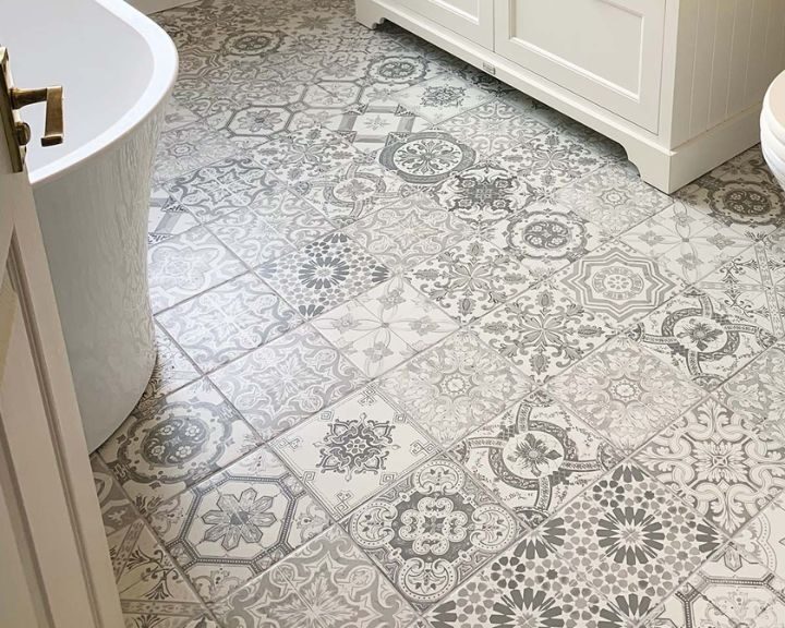 Patterned mosaic tiling bathroom floor tiles with a freestanding bathtub and white vanity cabinet.