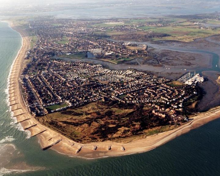 Aerial view of a coastal town with residential areas adjacent to a beach and a river estuary, featuring extensive porcelain tiling.