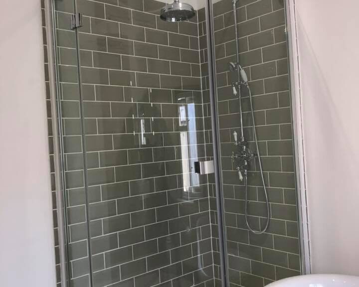 A corner shower stall with glass doors and grey porcelain tiling.