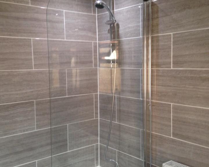 A modern bathroom with a glass shower partition over a bathtub, natural stone tiling on the walls, and a wall-mounted showerhead.