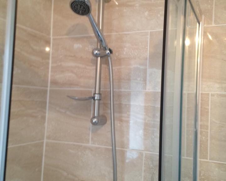 A modern shower with a height-adjustable showerhead, glass door, and porcelain tiling.