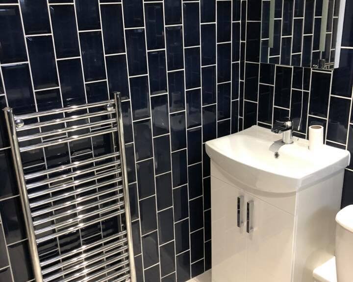 A modern bathroom corner with porcelain tiling, a pedestal sink, and a heated towel rail.