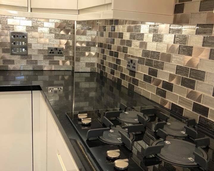 A modern kitchen with a black countertop, white cabinets, and a natural stone tiled backsplash, featuring a gas cooktop with pots and pans.